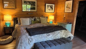 Un dormitorio acogedor con una cama grande, dos mesitas de noche con lámparas, un banco y cuadros enmarcados en las paredes.