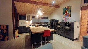 Una cocina moderna con vigas de madera, una isla central y un comedor con una silla roja.