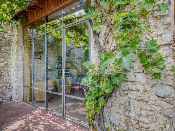 Un edificio de piedra con puerta de cristal que da a una zona de estar al aire libre con mobiliario de mimbre.