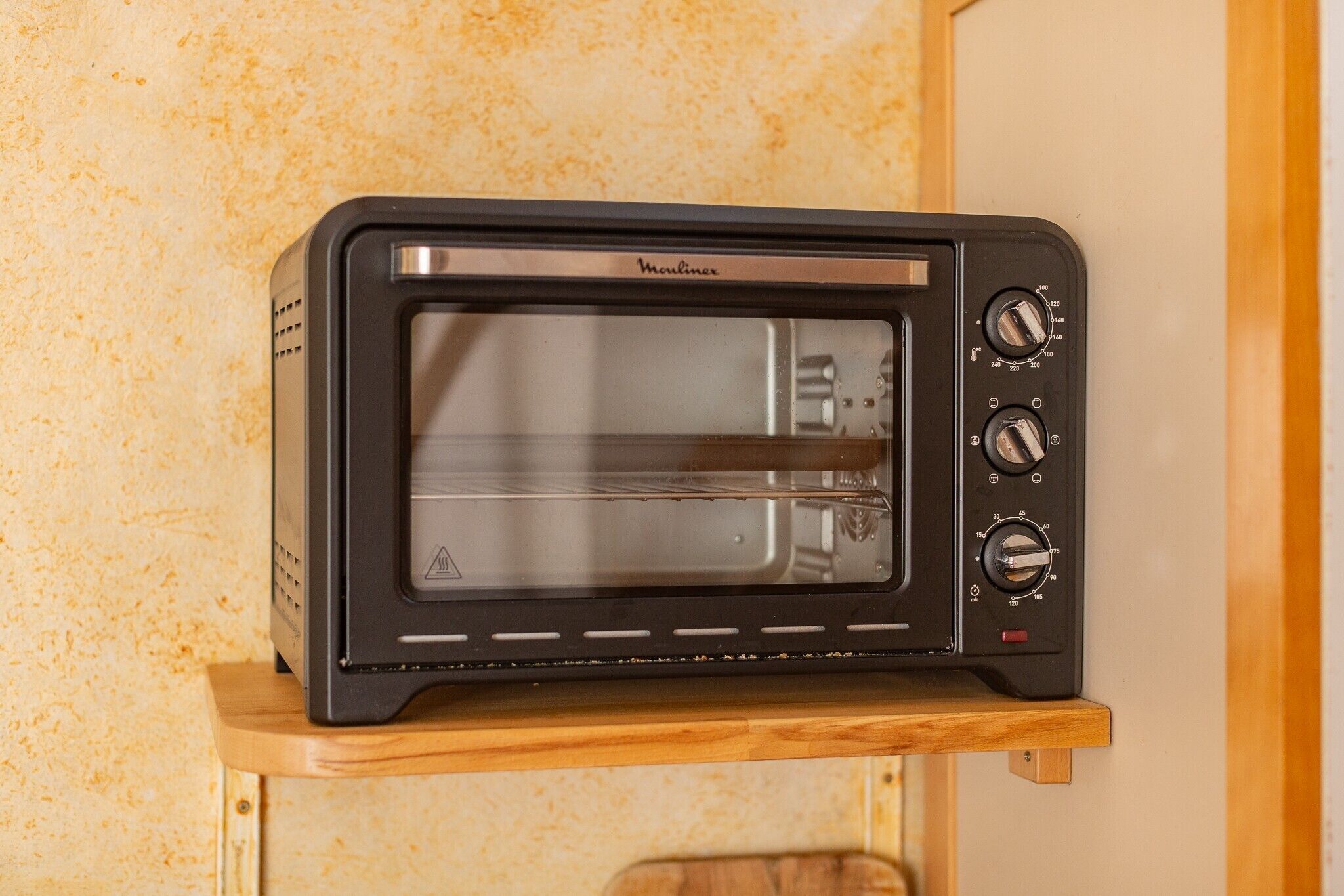 A black toaster oven with a control panel on a wooden shelf.