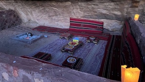 Interior de caverna com lareira, espaço de estar e mesa com comida.