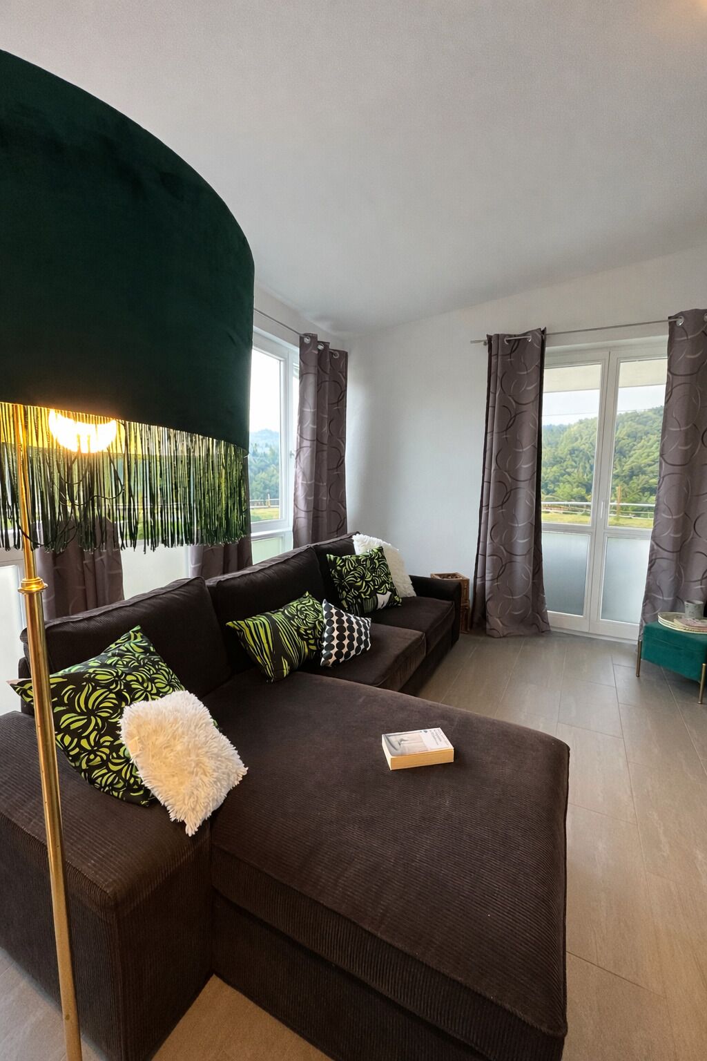A modern living room with a dark brown sectional sofa, patterned cushions, a white fluffy throw, and a floor lamp.