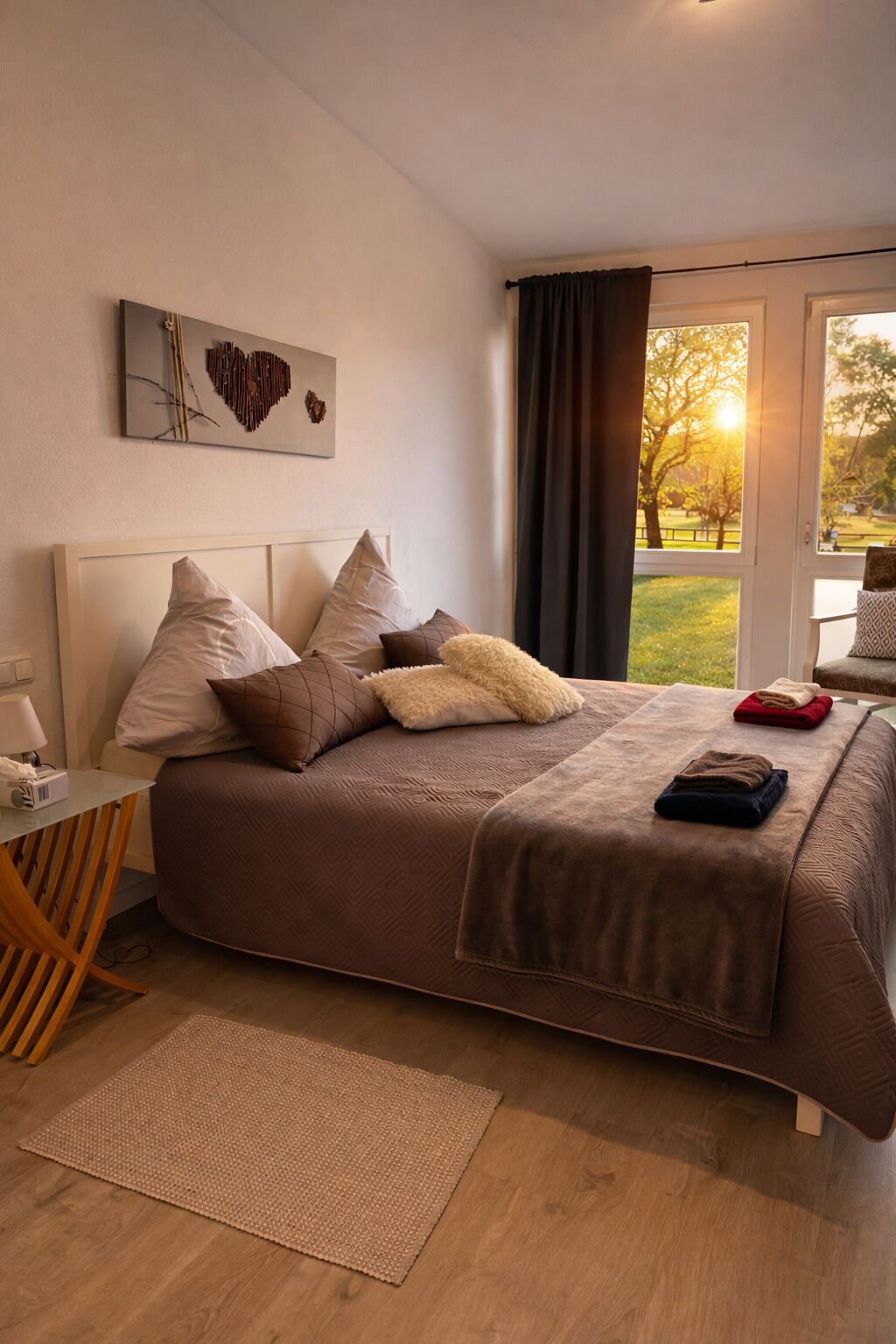 A bedroom with a large bed, a desk, and a view of a park through a window.