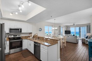 A modern kitchen with a central island, stainless steel appliances, and a view to the ocean. - Ariel Dunes 901 Gulf view condo in Destin at Seascape Resort (Miramar Beach)