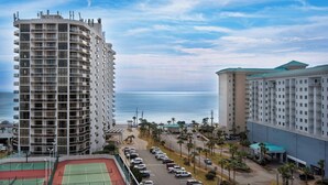 Un hotel di grandi dimensioni con numerosi balconi, un campo da tennis e vista sull'oceano.
