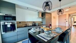 A modern kitchen with stainless steel appliances, a central island with seating, and pendant lighting. - Le Mistral - Elegant apartment with sea view! (Le Grau-du-Roi)