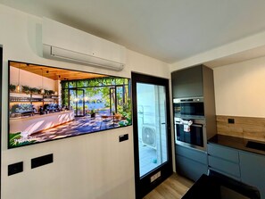 Eine moderne Küche mit integrierten Geräten, einem großen Fenster mit Blick auf Grünflächen und einer Wand-Klimaanlage.