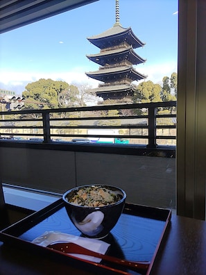 A dining table with a bowl of food and chopsticks, a window with a view of a pagoda, and a railing.