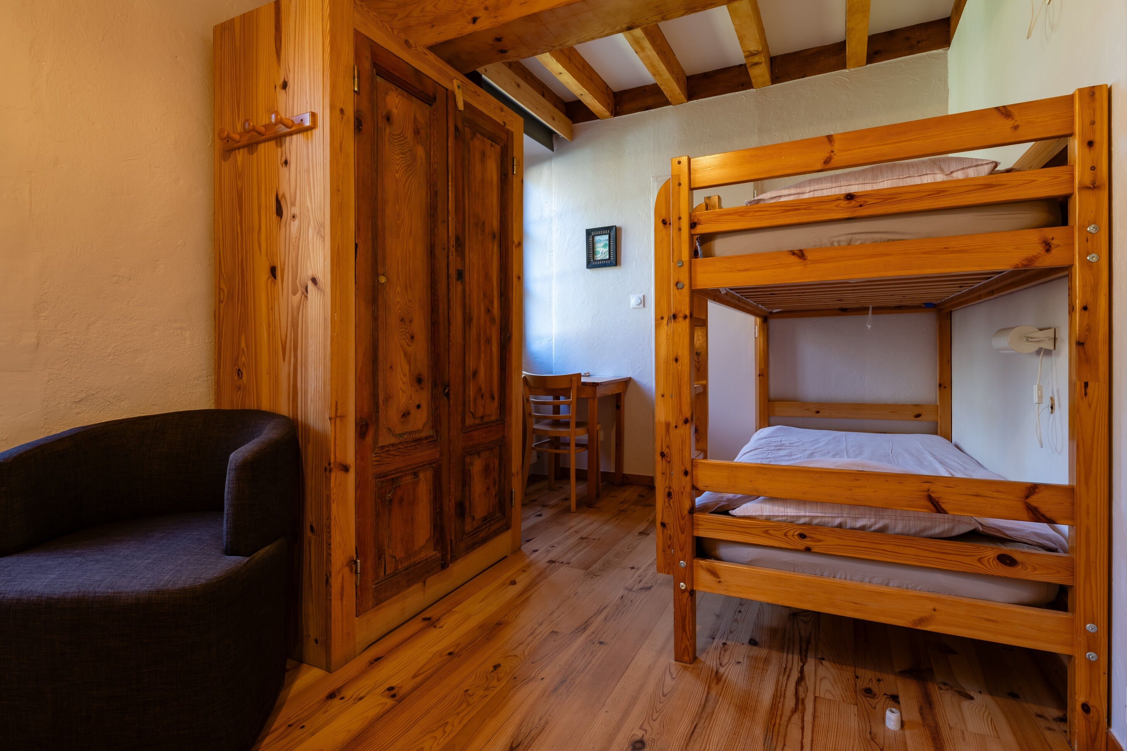 Ein Holzbett mit Etagen, ein Holzschrank und ein dunkel gefärbter Stuhl in einem Raum mit Holzboden und geneigter Decke.