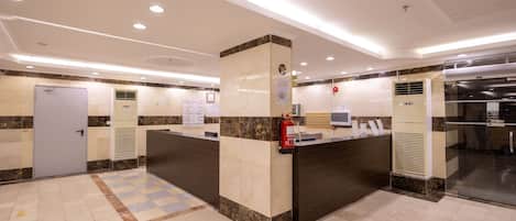 Ein Hotel-Empfangsbereich mit einer Rezeption, einem Feuerlöscher und einer Glastür zum Küchenbereich.