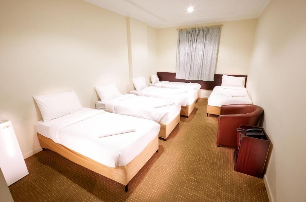 Een hotelkamer met drie eenpersoonsbedden, een slaapbank en een kleine tafel.