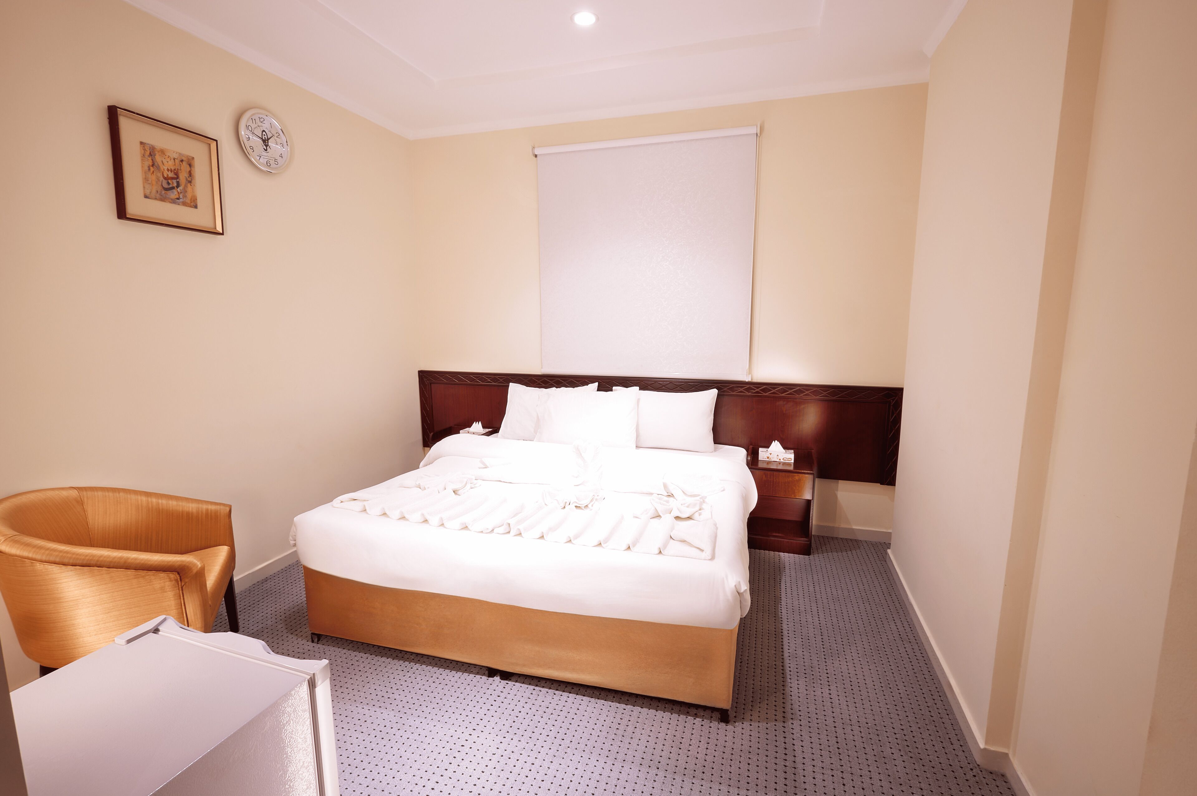 Een hotelkamer met een groot bed, een houten hoofdbord, een nachtkastje, een stoel en een wandklok.