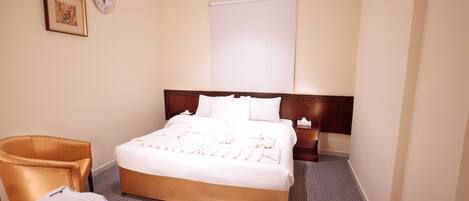 Een hotelkamer met een groot bed, een houten hoofdbord, een nachtkastje, een stoel en een wandklok.
