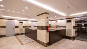 A hotel reception area with a marble counter, a fire extinguisher, and a glass door leading to a kitchen. - Al Zaireen 2 (Makkah)