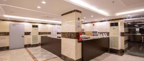 A hotel reception area with a marble counter, a fire extinguisher, and a glass door leading to a kitchen.