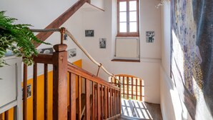 A wooden staircase with a rope handrail, a window with a radiator, and a wall with framed pictures. - Guesthouse “La Chastanha - Room 2” with Mountain View (Saint-Symphorien de Mahun)