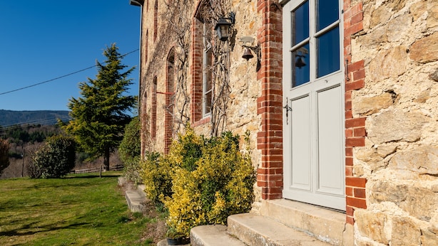 A stone building with a white door, steps leading up to the entrance, and a small garden area with bushes. - Guesthouse “La Chastanha - Room 2” with Mountain View (Saint-Symphorien de Mahun)