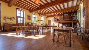 A spacious room with wooden floors, a high ceiling with exposed beams, a dining area with tables and chairs, and a loft with a balcony. - Guesthouse “La Chastanha - Room 2” with Mountain View (Saint-Symphorien de Mahun)