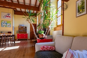 Un salon chaleureux avec un plancher en bois, un buffet rouge, un canapé blanc et une grande plante en pot.