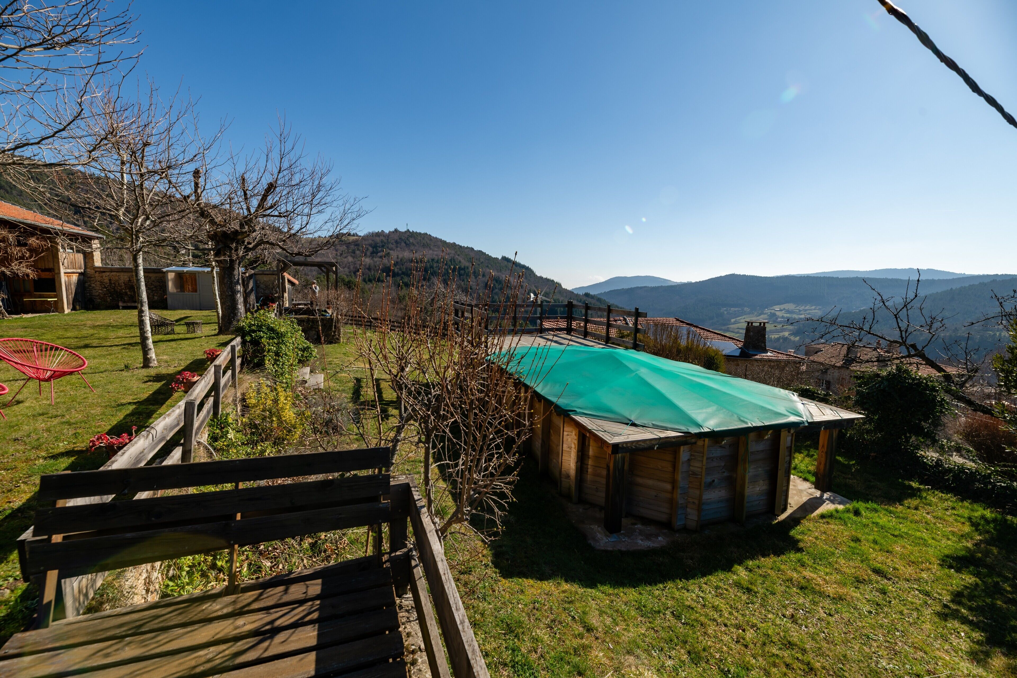 A wooden cabin with a green roof, surrounded by a wooden deck and a red chair.