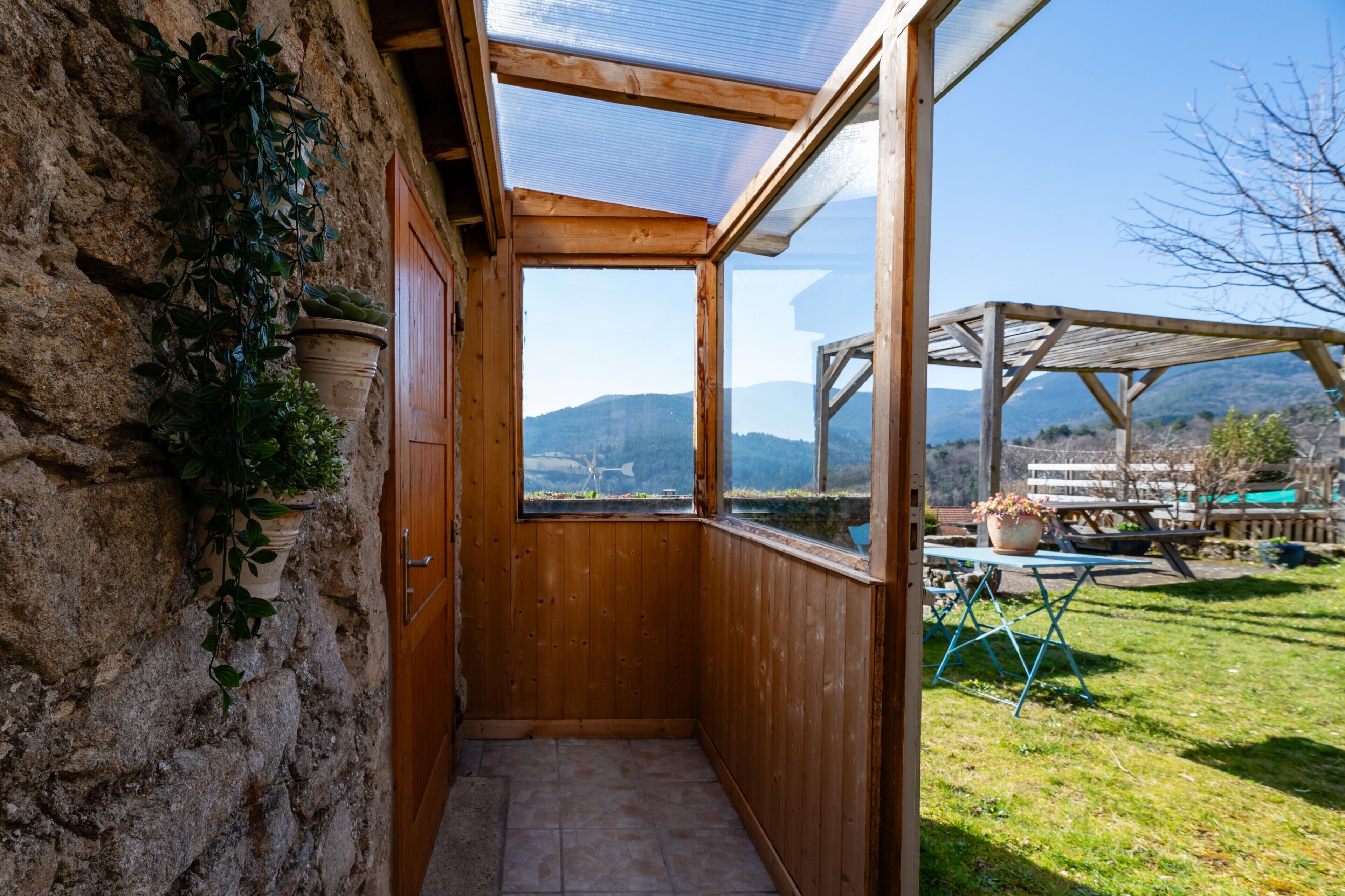 A wooden room with a view of mountains, a wooden table with a potted plant, and a stone wall.