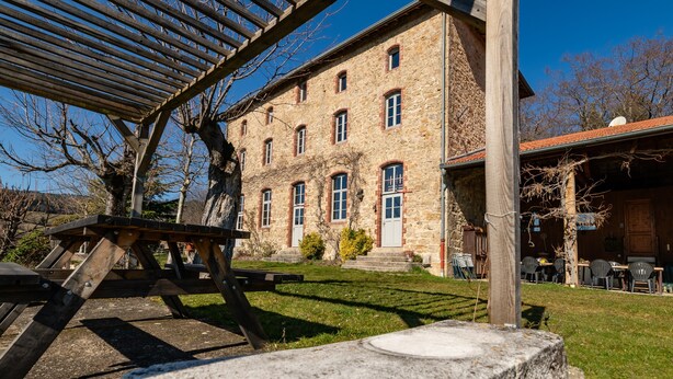 A stone building with multiple windows and a covered outdoor area with tables and chairs. - Eco-Lodge Cabin in Ardèche Close to Nature (Saint-Symphorien de Mahun)