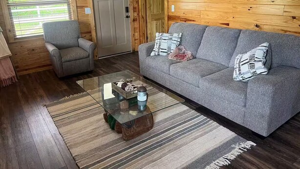 A cozy living room with a grey sofa, a grey armchair, and a glass coffee table. - Sowell’s Cozy Cottage (Milton)