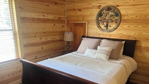 A wooden-paneled bedroom with a bed, a wall-mounted lamp, and a decorative tree piece. - Sowell’s Cozy Cottage (Milton)