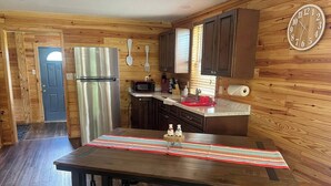 A kitchen with wooden walls, a stainless steel refrigerator, a microwave, and wooden cabinets. - Sowell’s Cozy Cottage (Milton)