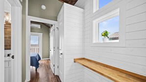 A narrow hallway with white paneled walls and wooden flooring. A window with a plant is visible on the right wall. - Pet-Friendly Tiny Home Near Beach & Marinas (Rockport)