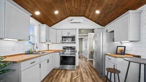 A modern kitchen with white cabinets, stainless steel appliances, wooden flooring, and a wooden ceiling. - Pet-Friendly Tiny Home with Boat Parking (Rockport)