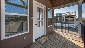 A wooden deck with a welcome mat, a door with a window, and a view of neighboring houses. - Pet-Friendly Tiny Home with Boat Parking (Rockport)