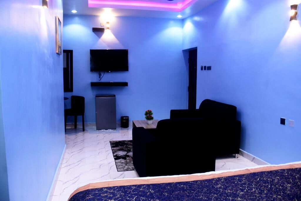 Una sala de estar moderna con una pared azul, un televisor de pantalla plana montado sobre un sofá oscuro, y una mesita con un florero.