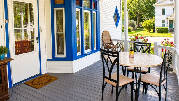 A covered porch with a round table and chairs, a door with blue trim, and a view of a green lawn and white house. - Sounds of the Waterfall - 1mi to Racetrack & Park (Montour Falls)