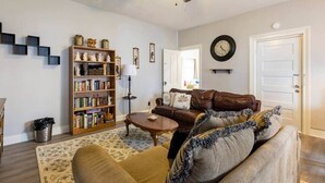 A living room with a brown leather sofa, a wooden bookshelf, a round coffee table, and a ceiling fan.
