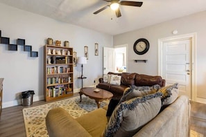 A living room with a brown leather sofa, a wooden bookshelf, a round coffee table, and a ceiling fan.