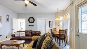 A living room with a brown leather sofa, a beige sofa, a wooden coffee table, a dining table with chairs, a ceiling fan, and a clock on the wall. - Sounds of the Waterfall - 1mi to Racetrack & Park (Montour Falls)