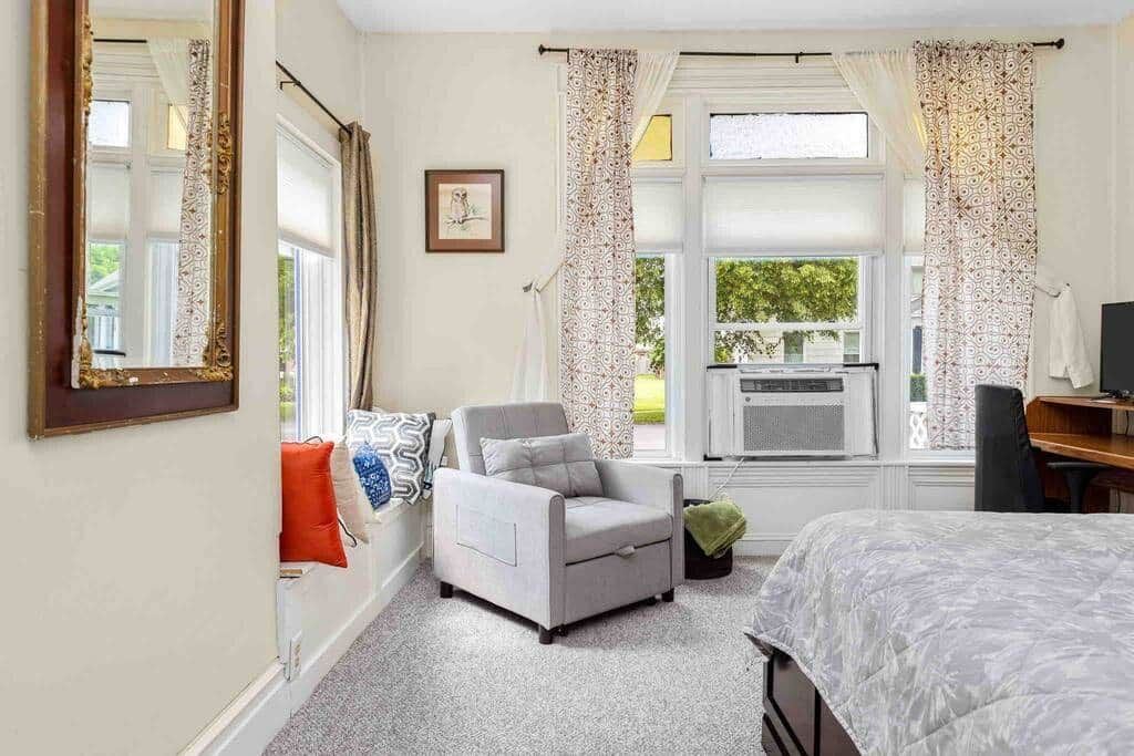 A bedroom with a bed, a chair, a desk, and a window with curtains.