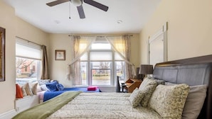 A bedroom with a large bed, a desk, a chair, a ceiling fan, and a window with curtains.