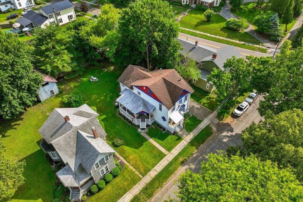 An aerial view of a residential area with a large house featuring a prominent gable roof and a smaller attached structure.