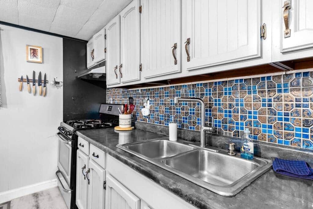 Una cocina con armarios blancos, salpicadero de azulejos, un lavamanos doble y una estufa.