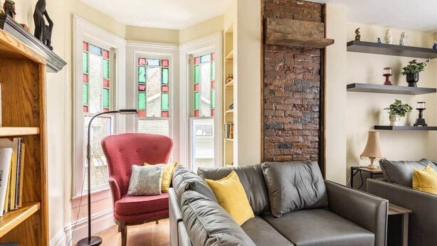Ein Wohnzimmer mit grauem Sofa, rotem Sessel und einer Wand aus Ziegelsteinen.