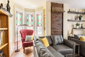 Una sala de estar con sofá gris, sillón rojo y pared de ladrillo decorativa.