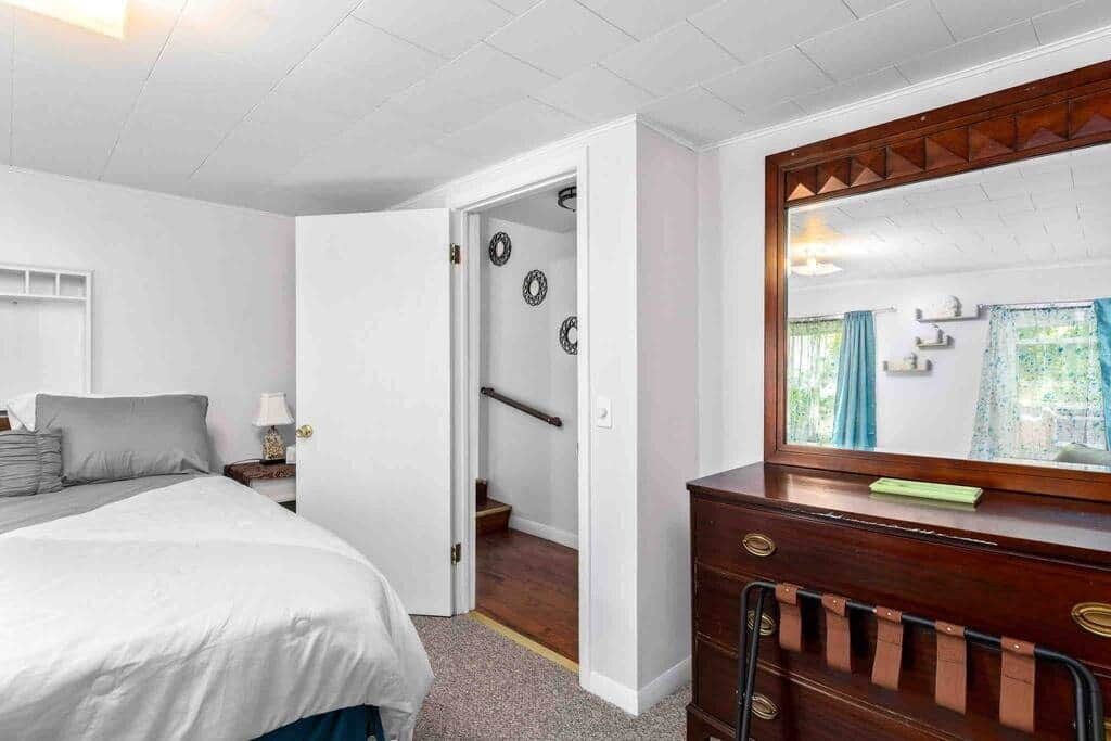Une chambre à coucher comprenant un lit, une commode, un miroir et une porte donnant sur un escalier.