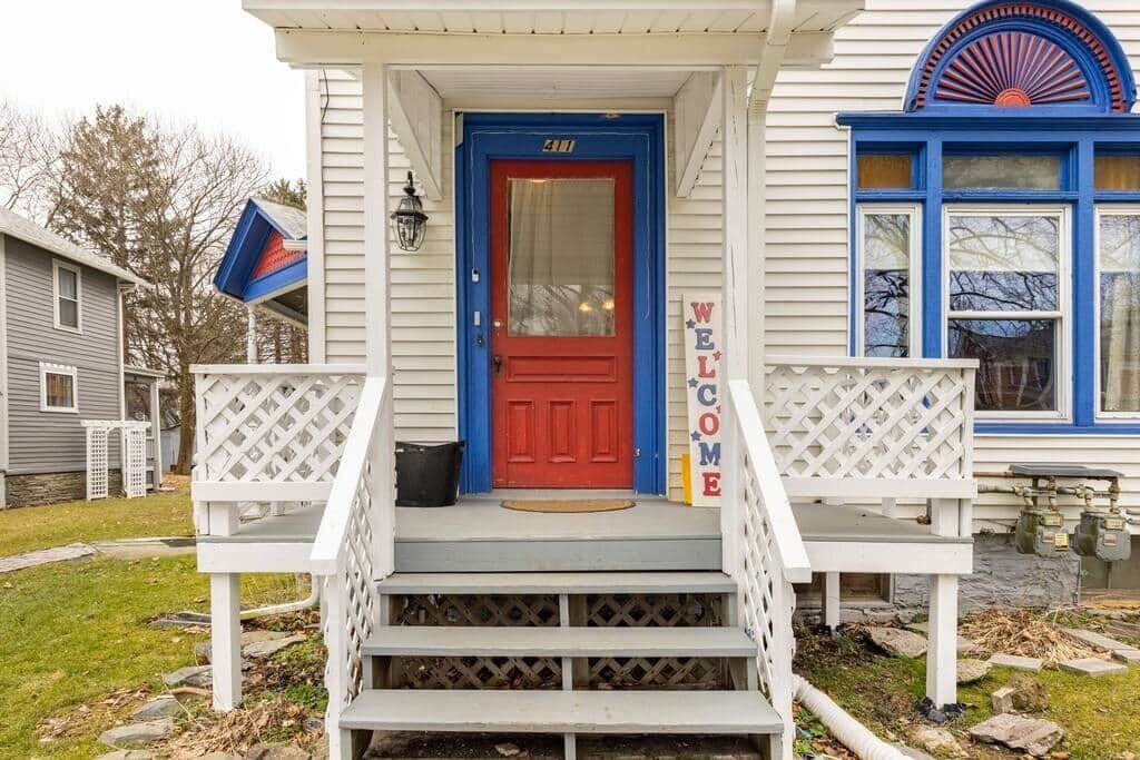 A house with a red door, a welcome sign, and a blue window.
