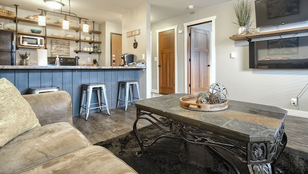 Una cocina moderna con barra, una mesa de comedor con un centro decorativo y una zona de estar acogedora con sofá y taburetes.