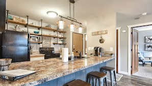 Una cocina con encimera de granito, electrodomésticos de acero inoxidable y taburetes de bar.