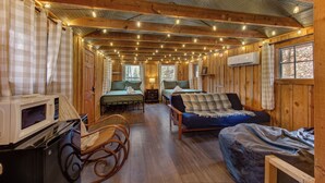 Interno di una baita con pareti in legno, un letto, un divano, un tavolo da pranzo e un forno a microonde.