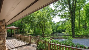 Un patio in legno con pavimento in pietra, un gazebo e uno stagno circondato da alberi.