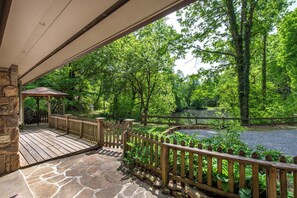 A wooden deck with stone flooring, a gazebo, and a pond surrounded by trees. - Private 10+ Acre Retreat | Hot Tub, Pond, Bunk House, and Peaceful Escape Near P (Sevierville)